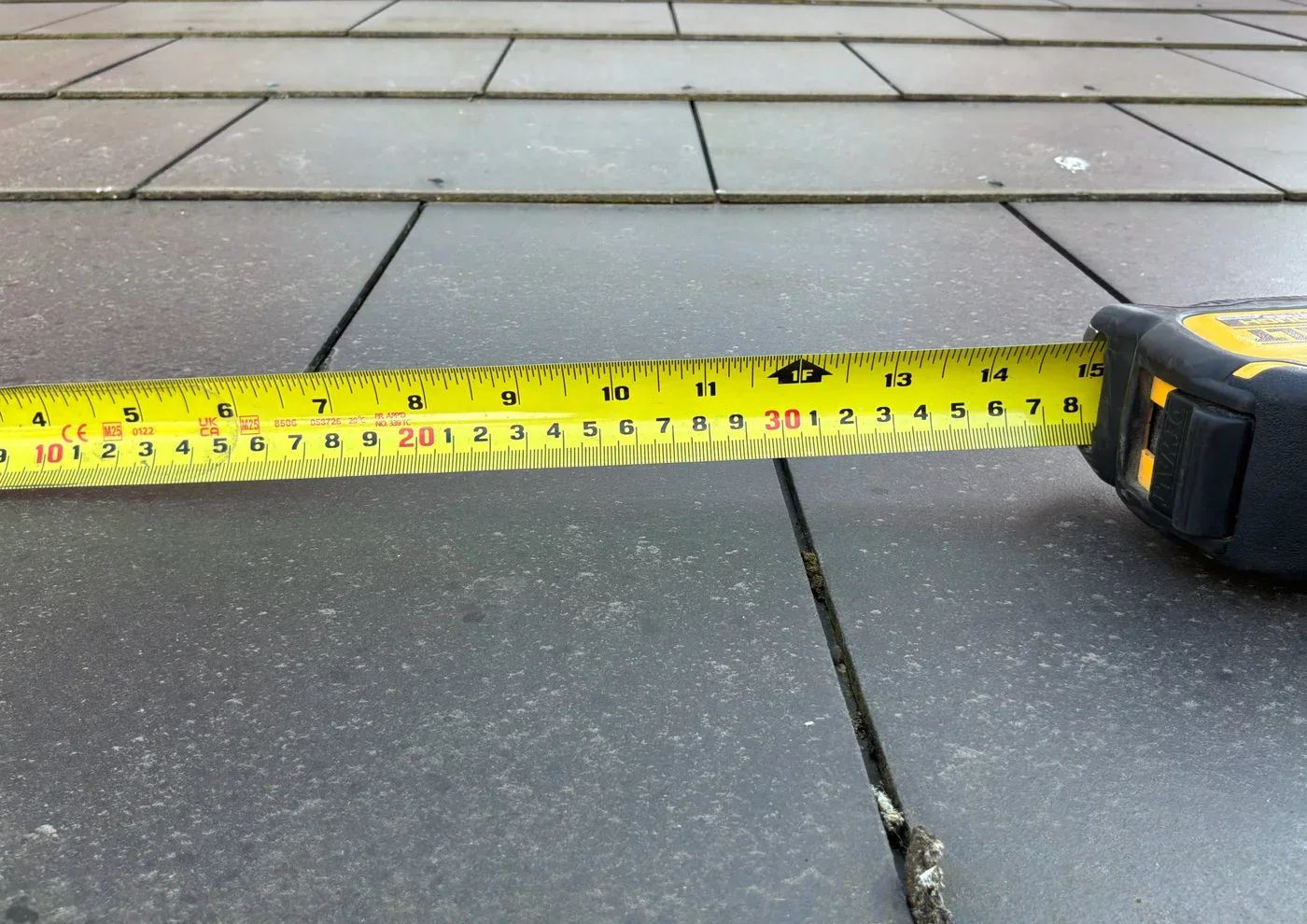 Tape measure placed across a man-made slate roof tile to show its width
